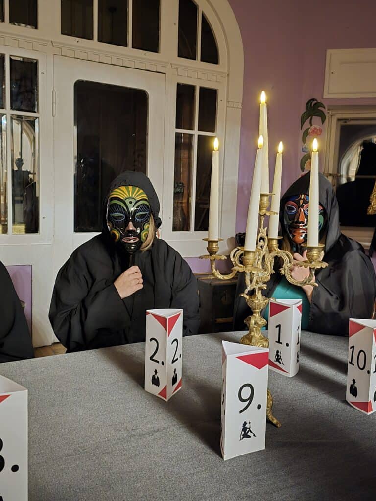 Two masked men play a game of mafia and parliament at a table with numbers and candlesticks.