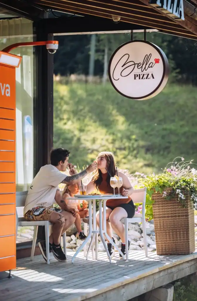 Family eating and laughing at a table outside Bella Pizza restaurant.