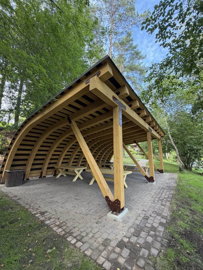 A picnic shelter with a wooden frame and wooden tables in Ramkalni.