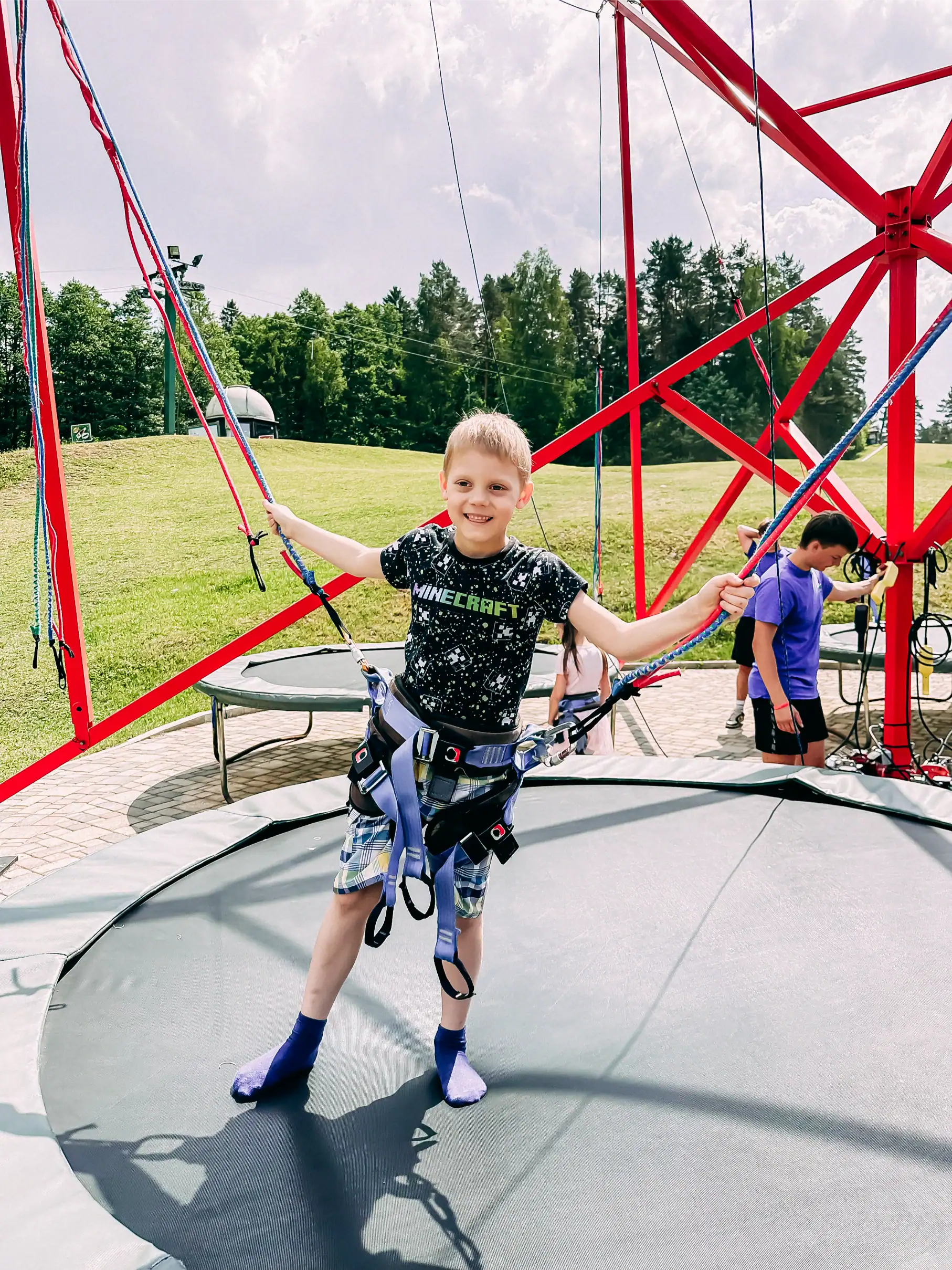 A child on a trampoline with amusement rides in the background in Ramkalni Park.