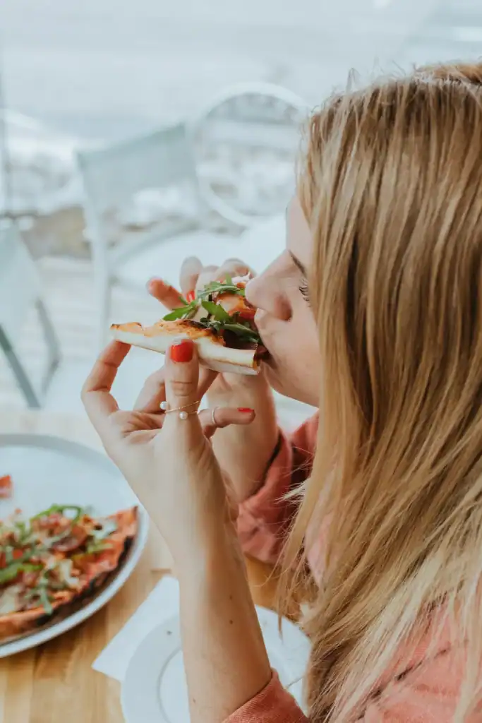 A woman is having a snack of vegetables and bread in a dining room with a white interior.
