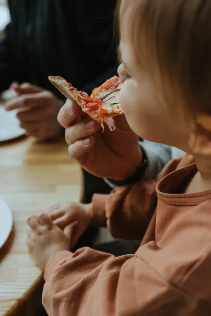 A child is eating a slice of pizza in the cosy atmosphere of a family dinner.