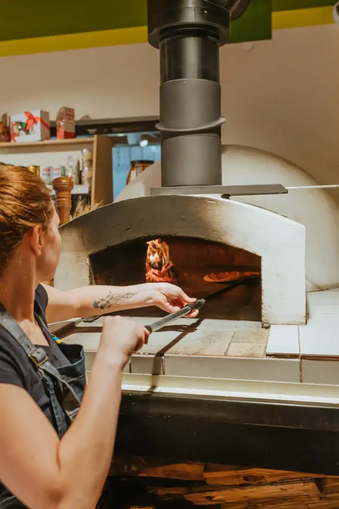 A woman bakes a pizza in a wood-fired oven at Ramkalni, a Latvian pizzeria and patisserie.
