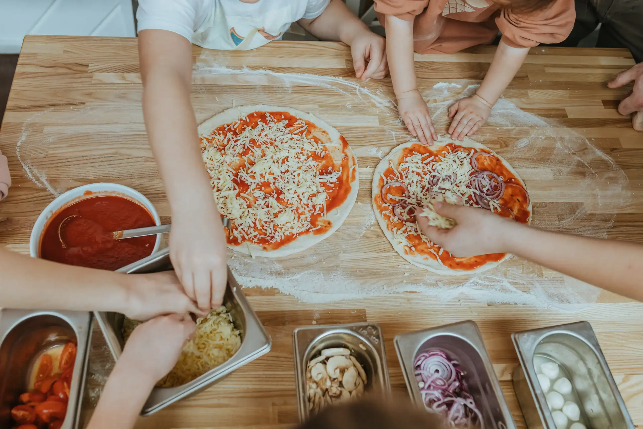 The children are working together to knead the dough as they make a pizza topped with cheese and tomatoes.
