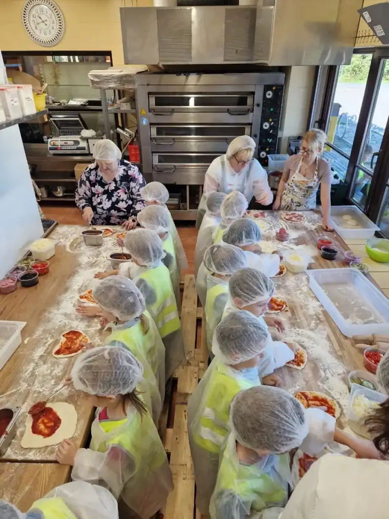 A group of children are baking pizzas together with the adults, learning and having fun.
