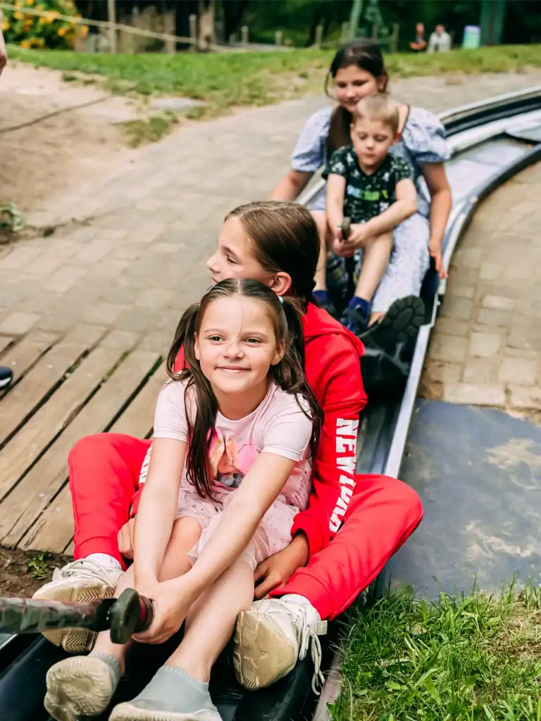 The children are enjoying a ride down the toboggan run in the park; a happy family together.