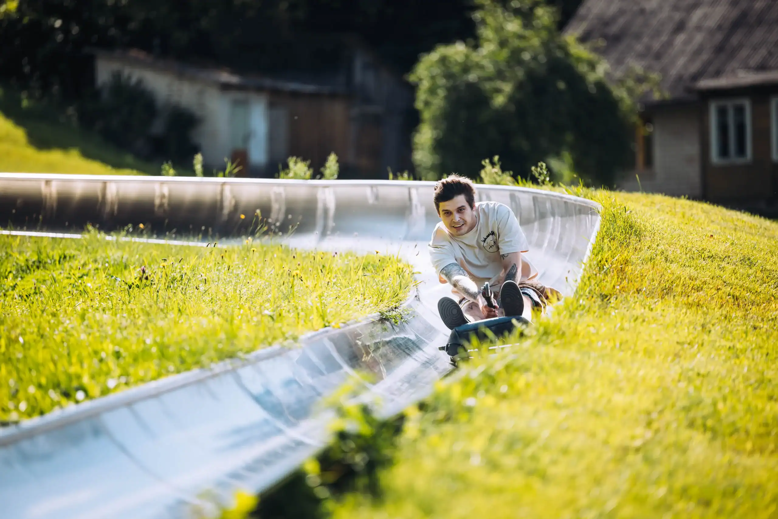 A child is sliding down a slide made of metal tyres, against a backdrop of green grass and houses.