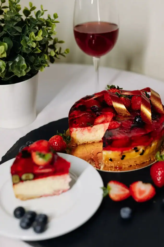A cheese and wine glass with a delicious fruit dessert, decorated with a golden ribbon and berries, on a white surface.
